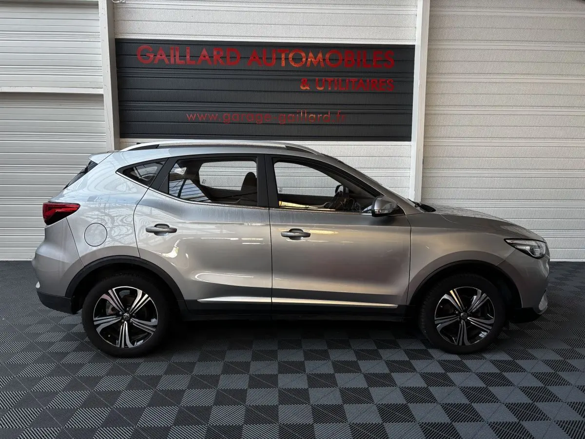 Vue de profil côté gauche d’un MG ZS gris clair 2022, SUV compact avec jantes alliage et barres de toit chromées.