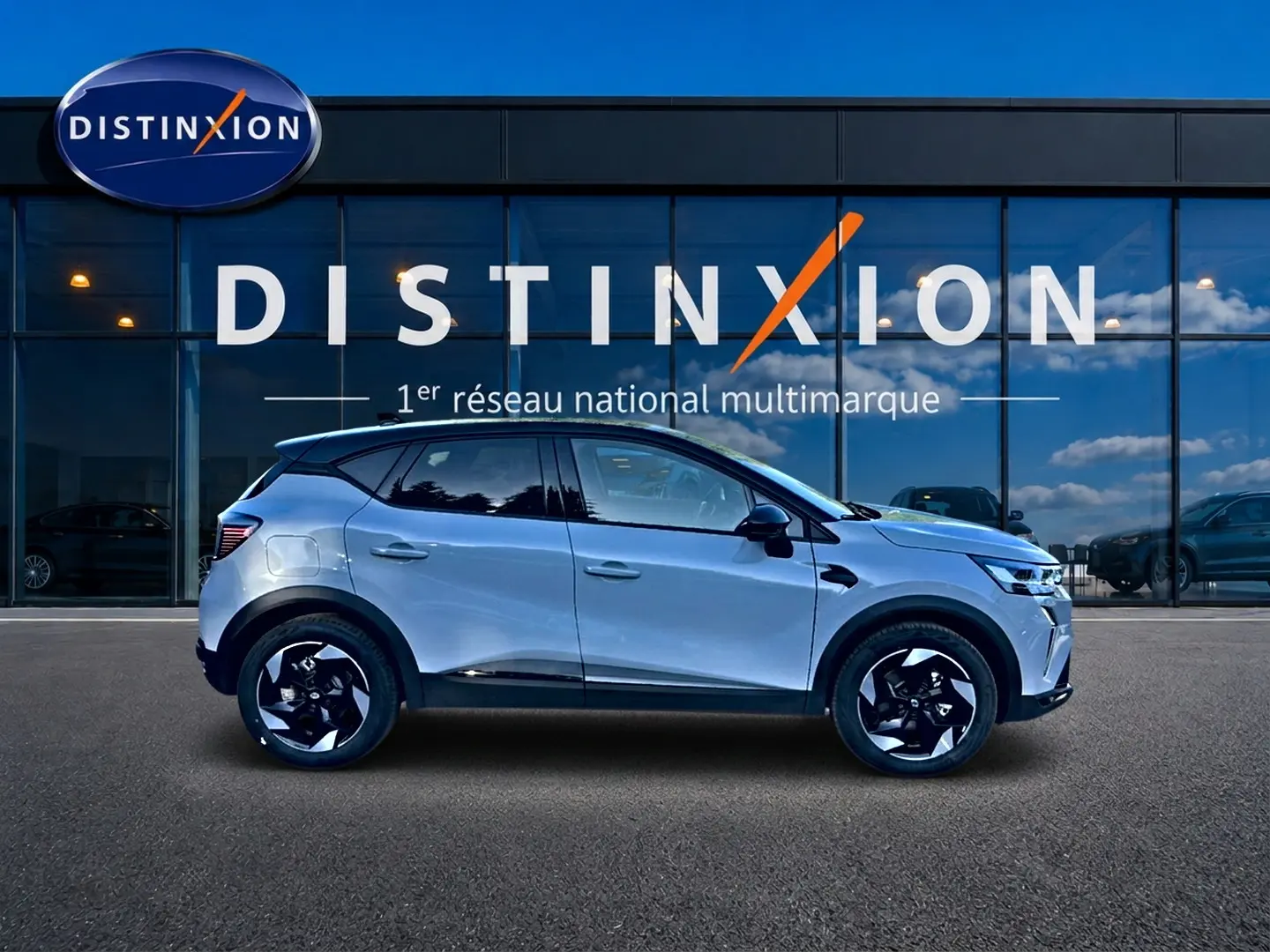 Profil droit du Renault Captur 2026 gris rafale avec jantes alu noires devant une vitrine Distinxion.
