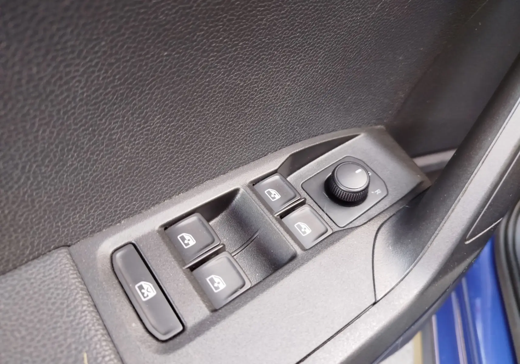 Gros plan sur les commandes de lève-vitres et réglage des rétroviseurs côté conducteur d'une SEAT Arona bleu électrique.
