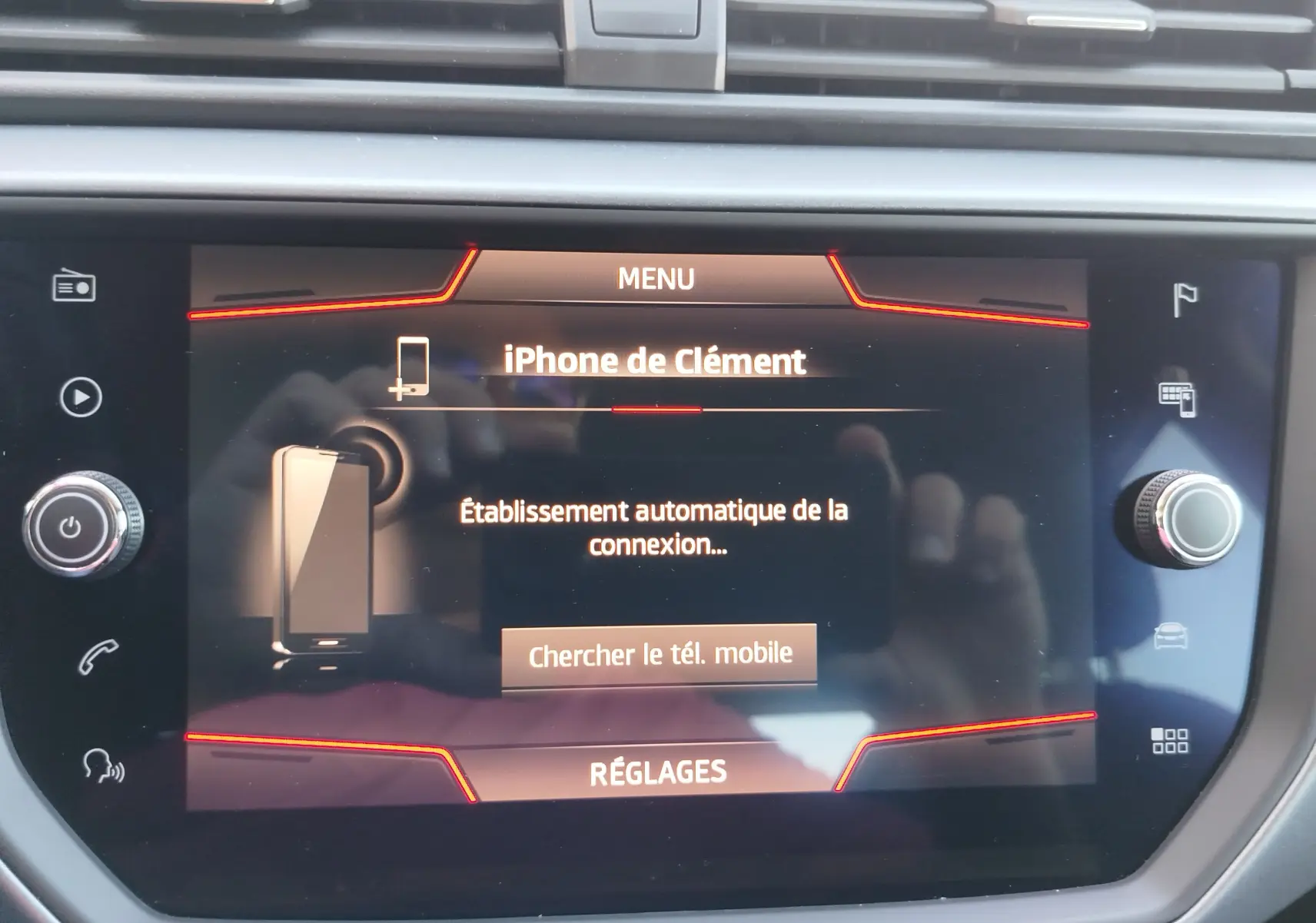Écran tactile central du SEAT Arona 2019 affichant la connexion Bluetooth à un iPhone, avec cadre noir et boutons lumineux rouges.