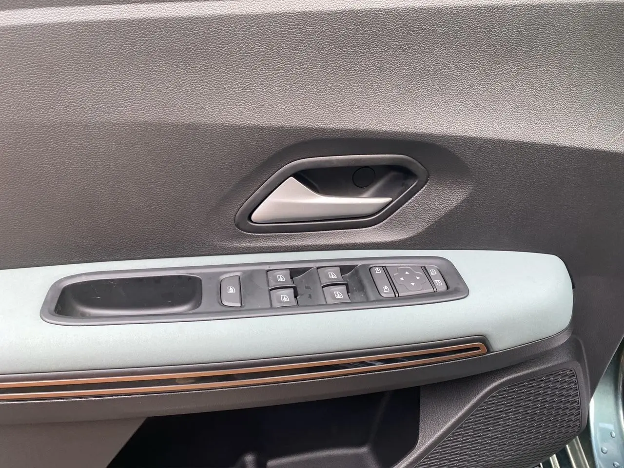 Détail de la porte côté conducteur du Dacia Sandero Stepway Vert Cèdre avec commandes des vitres et poignée intérieure grise.