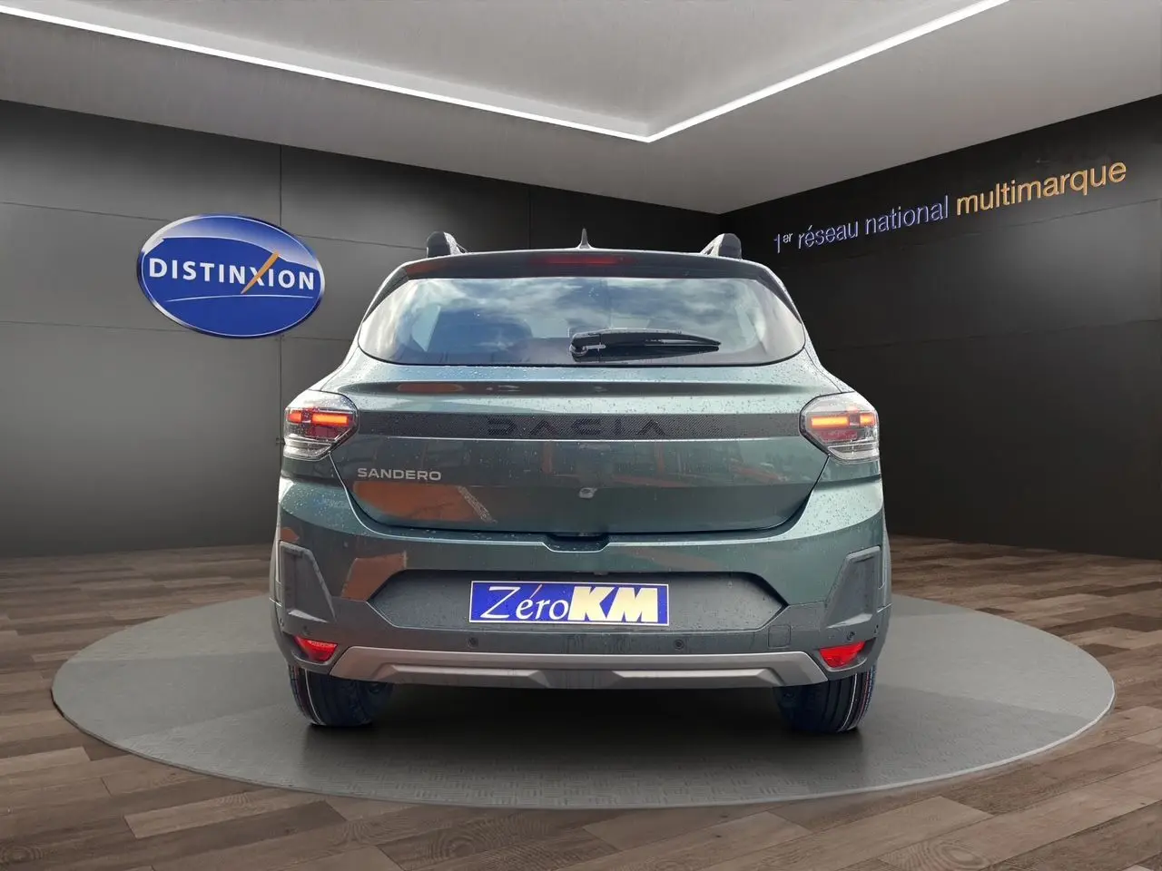 Vue arrière d'une Dacia Sandero Stepway 2026 en Vert Cèdre, avec feux allumés et plaque Zero KM visible.