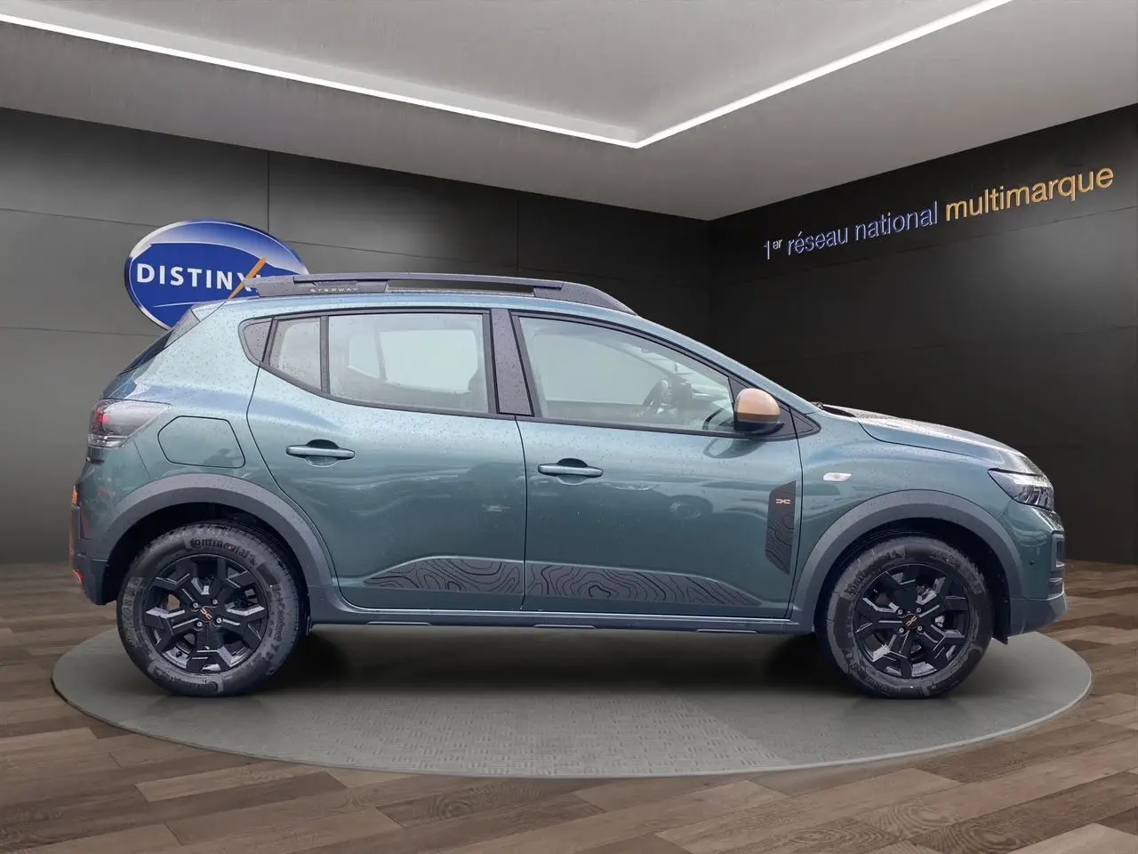 Vue de profil côté gauche d'une Dacia Sandero Stepway 2026 vert cèdre avec jantes alliage noires et barres de toit.