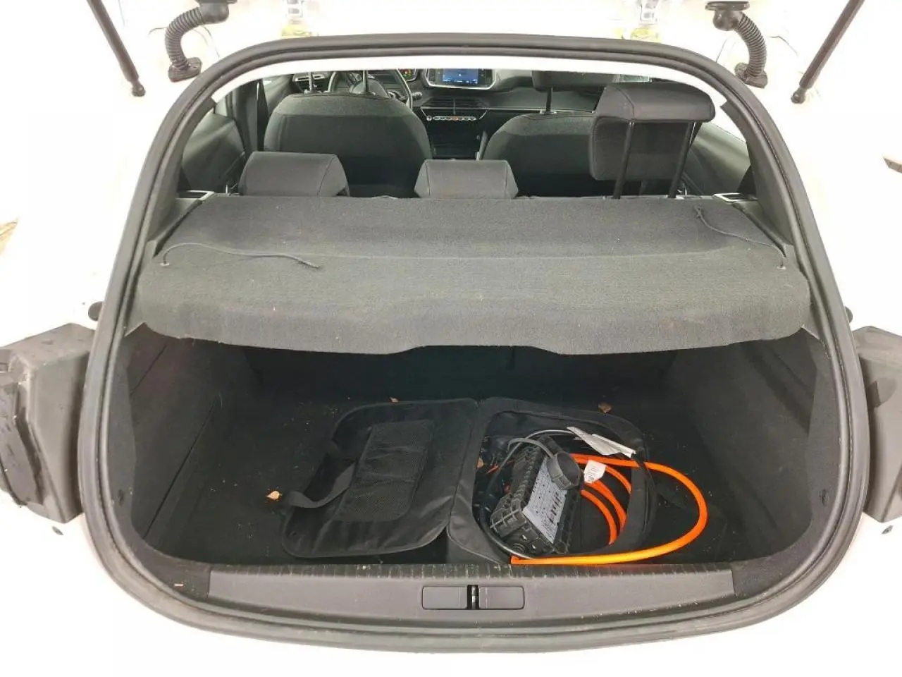 Vue arrière du coffre ouvert d'une Peugeot 208 électrique blanche avec câble de recharge visible à l'intérieur.