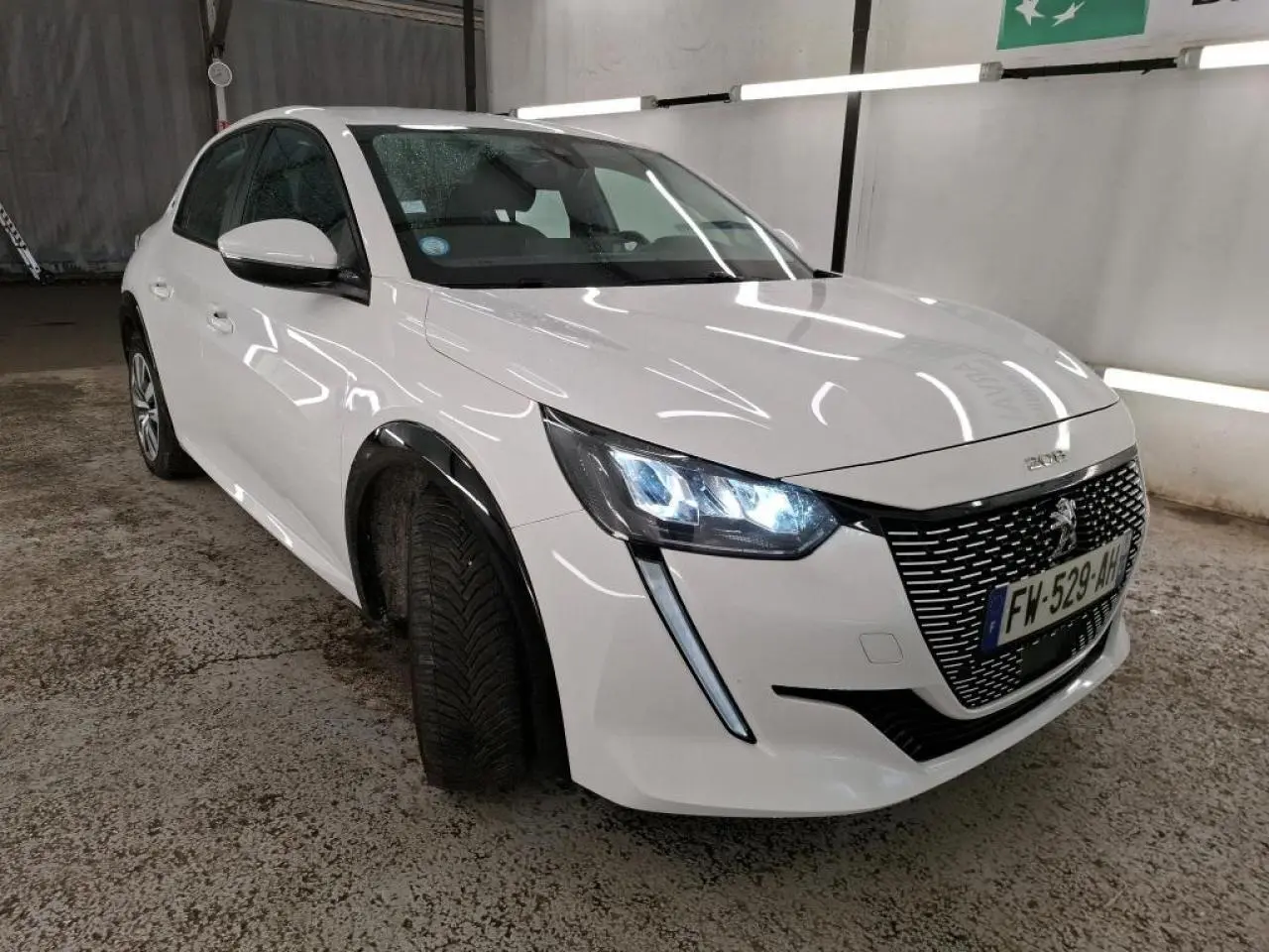 Peugeot 208 électrique blanc banquise vue 3/4 avant droit avec phares LED allumés en intérieur.