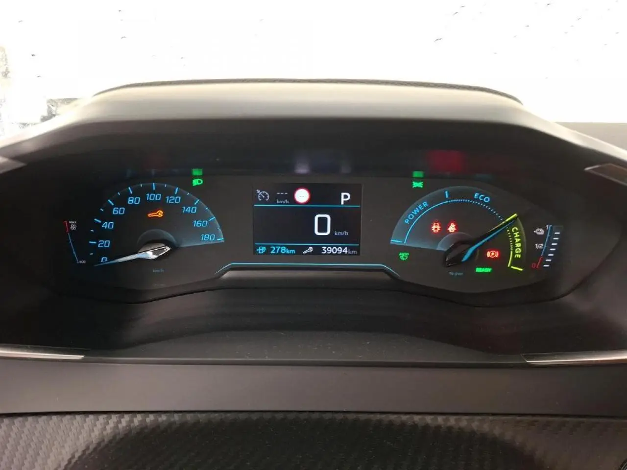 Vue rapprochée du combiné d'instruments numérique de la Peugeot 208 e-136 blanche, affichant 0 km/h et 27 8 km d'autonomie.