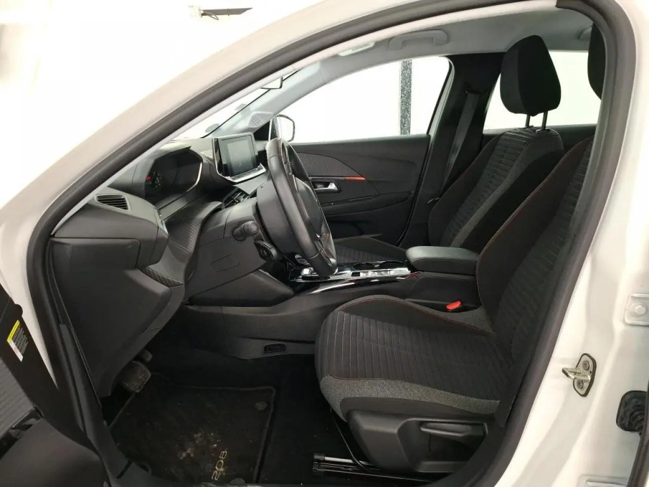 Vue intérieure côté conducteur d'une Peugeot 208 électrique blanche, sièges tissu noir avec surpiqûres orange et tableau de bord moderne.