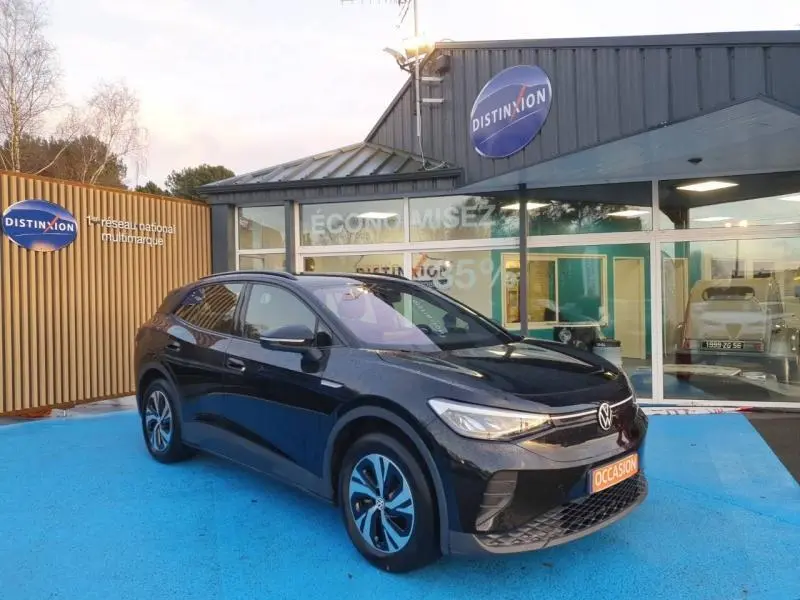Volkswagen ID.4 148ch Pure noir Ebène métallisé en 3/4 avant droit sur sol bleu devant un showroom Distinxion.