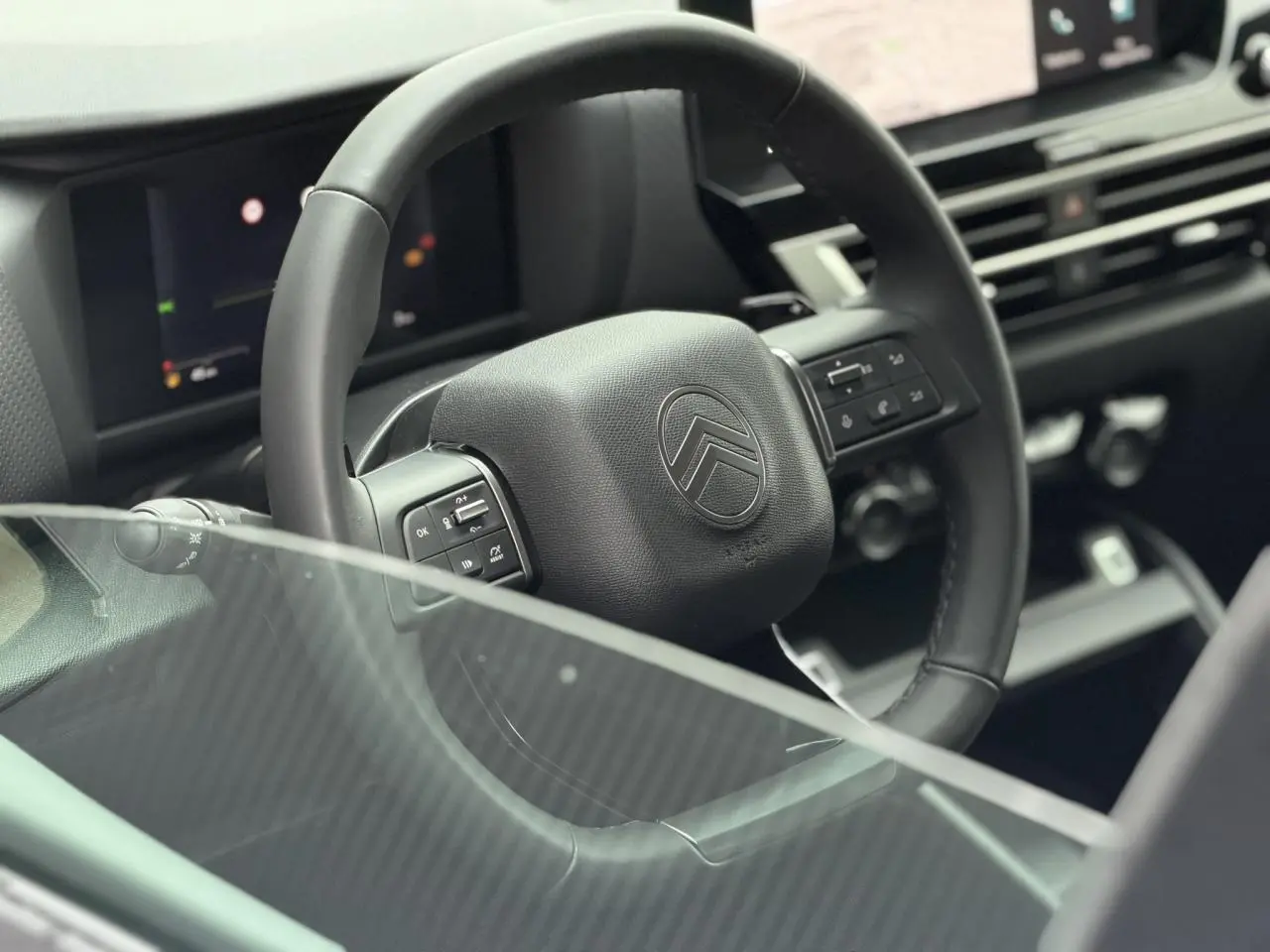 Vue rapprochée du volant noir de la Citroën C4 2025, avec commandes intégrées et tableau de bord numérique flou en arrière-plan.