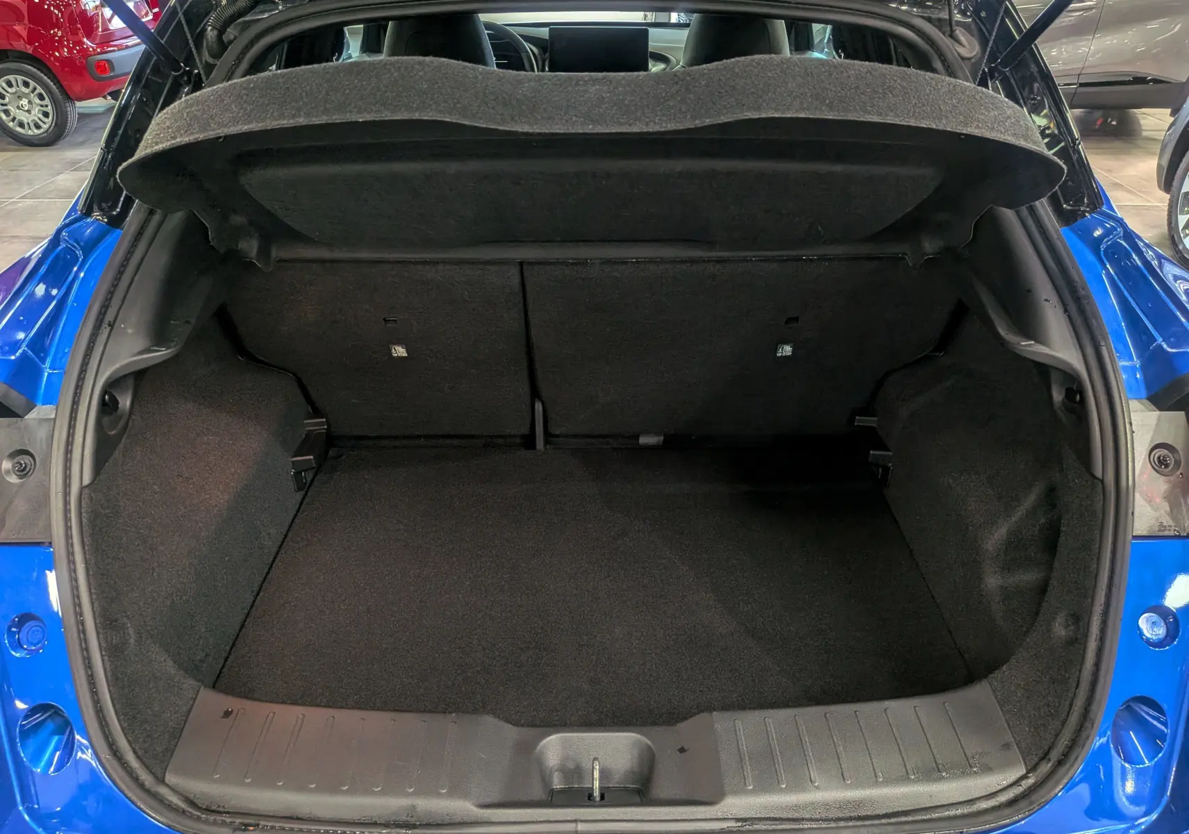 Coffre ouvert vu de l'arrière d'un Nissan Juke Hybrid 2025 bleu magnétique avec toit noir, intérieur de coffre vide et propre.