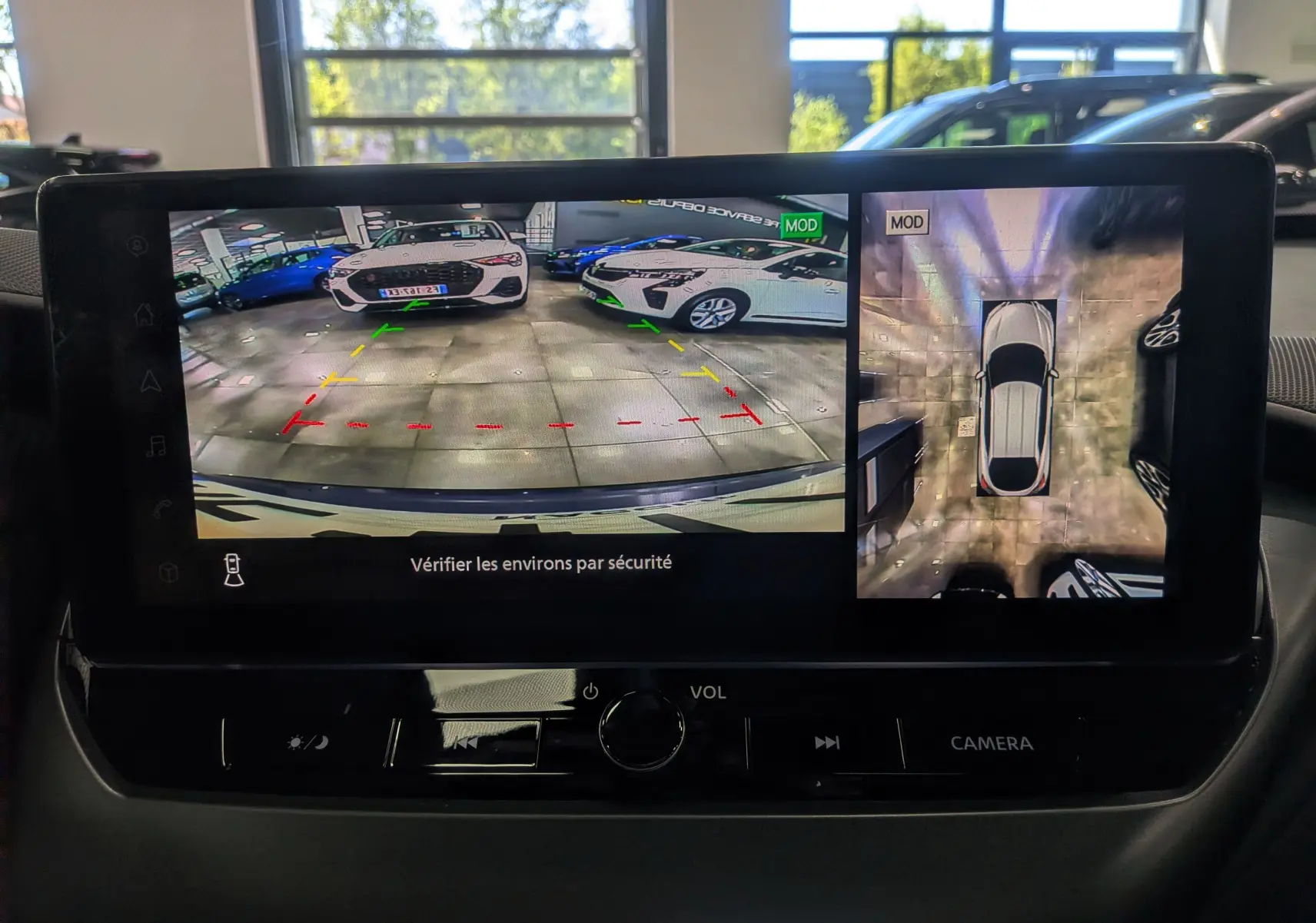 Écran intérieur du Nissan Juke Hybrid 2025 montrant la caméra de recul et la vue 360° avec le véhicule en bleu magnétique et toit noir.