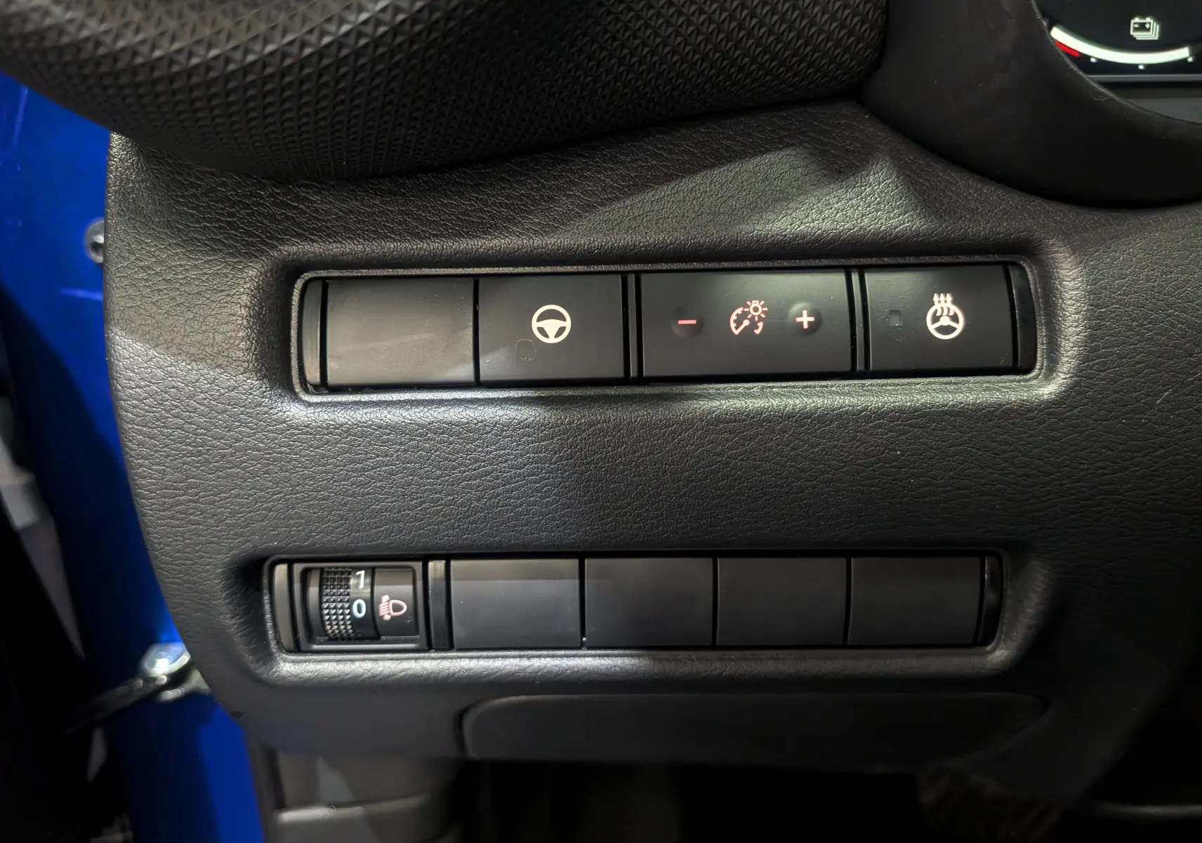 Gros plan sur les commandes de réglage du volant, éclairage et siège chauffant du Nissan Juke bleu magnétique 2025.