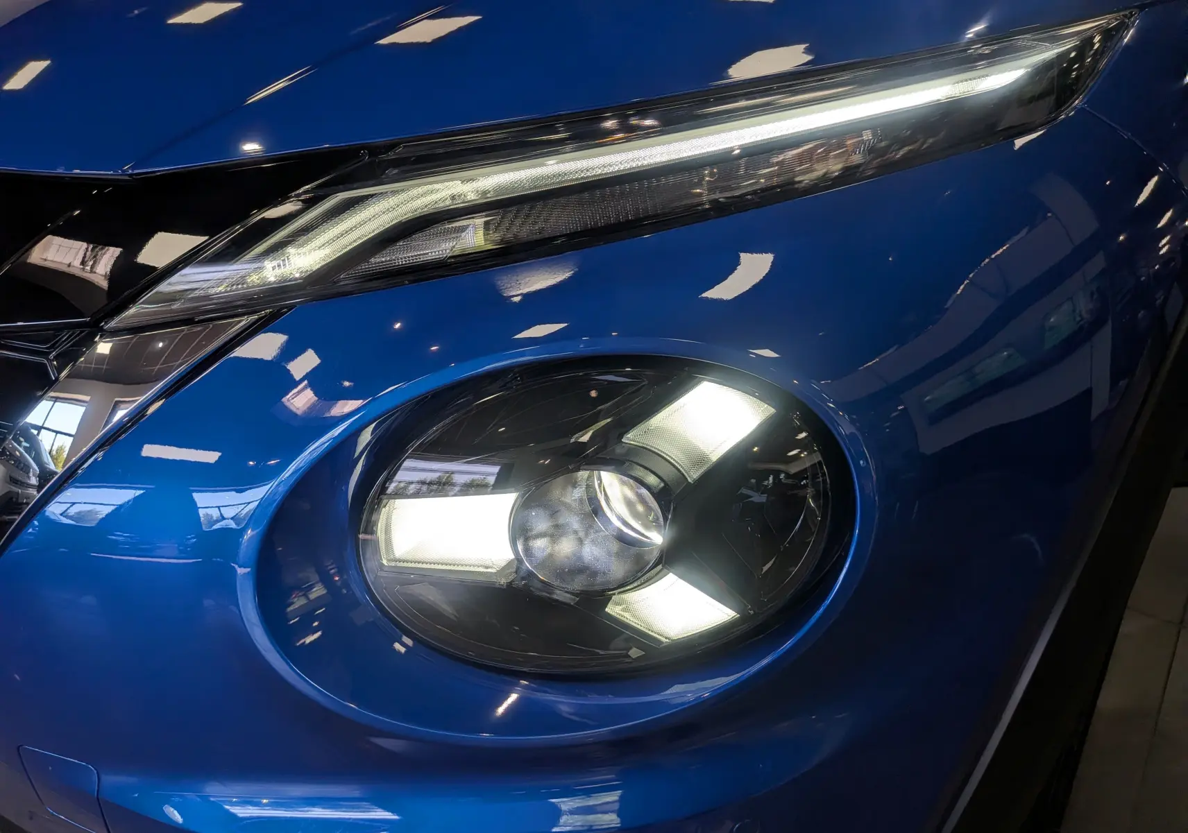 Gros plan sur le phare avant droit du Nissan Juke 2025 bleu magnétique avec toit noir, mettant en valeur son design lumineux distinctif.