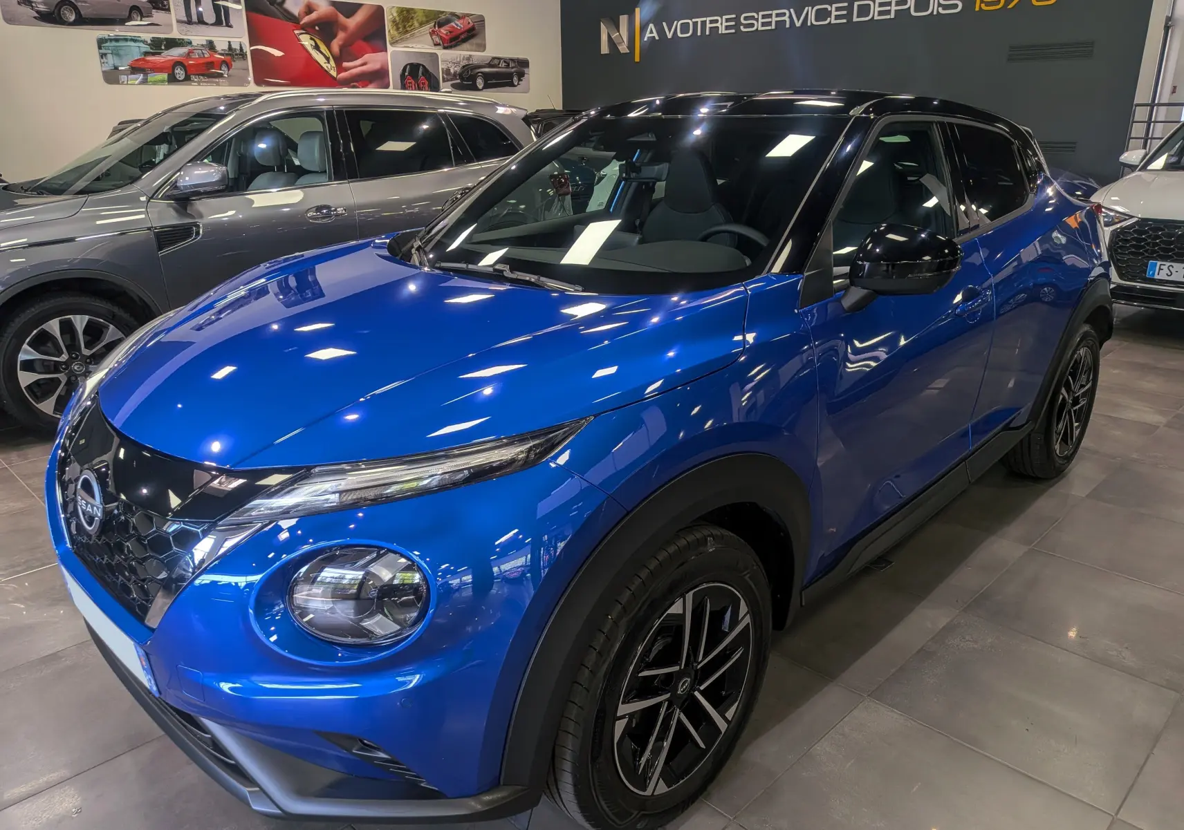 Nissan Juke Hybrid 2025 en bleu magnétique avec toit noir, vue 3/4 avant droit en intérieur showroom.