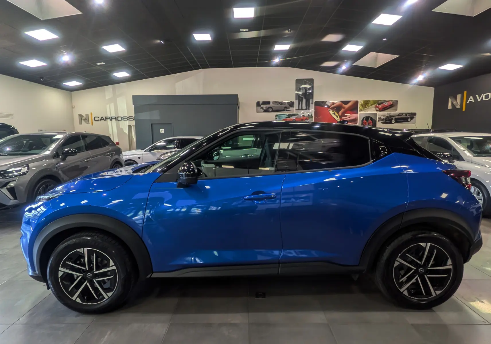 Vue de profil côté gauche d'un Nissan Juke Hybrid 2025 bleu magnétique avec toit noir et jantes alliage bicolores.