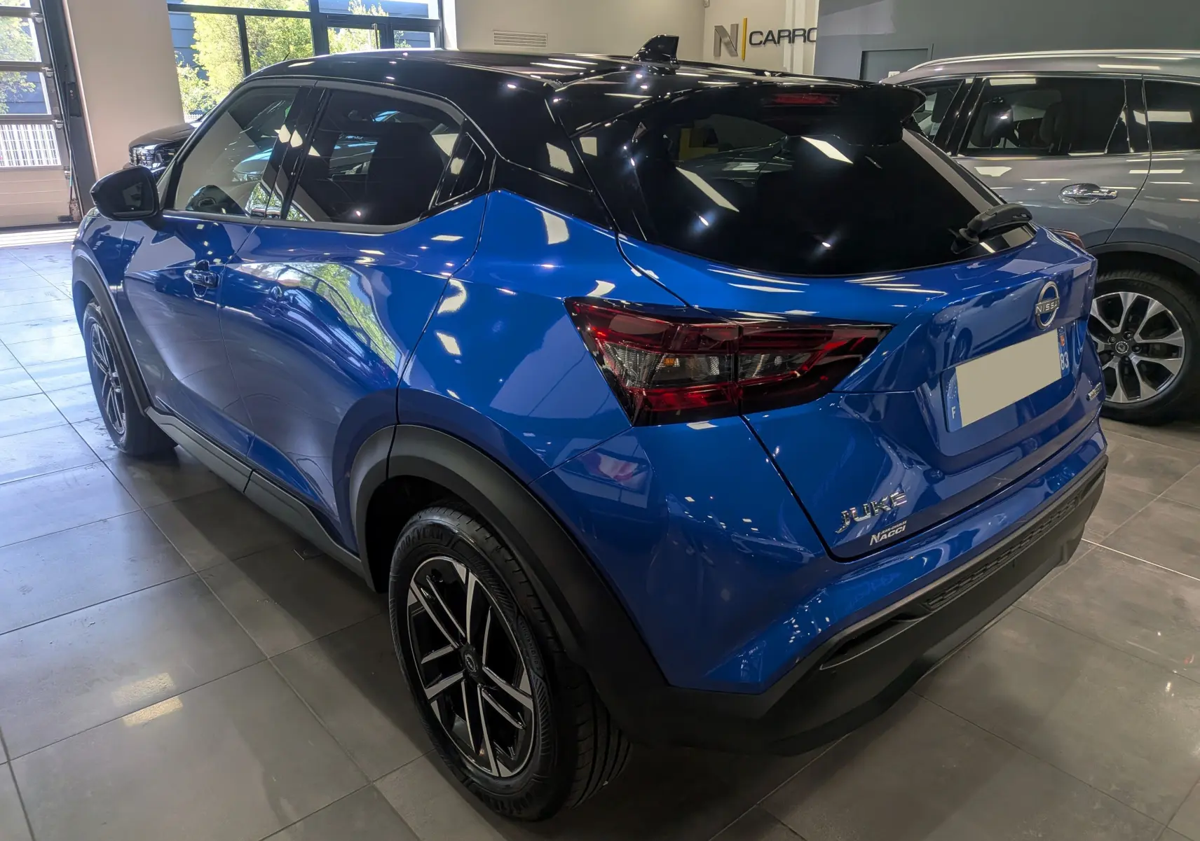 Vue 3/4 arrière droite du Nissan Juke Hybrid 2025 bleu magnétique avec toit noir et jantes noires en concession.