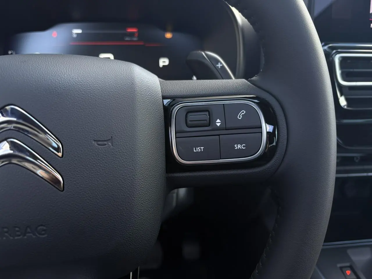 Gros plan sur le volant noir du Citroën C5 Aircross 2025, avec commandes intégrées et logo chromé visible.