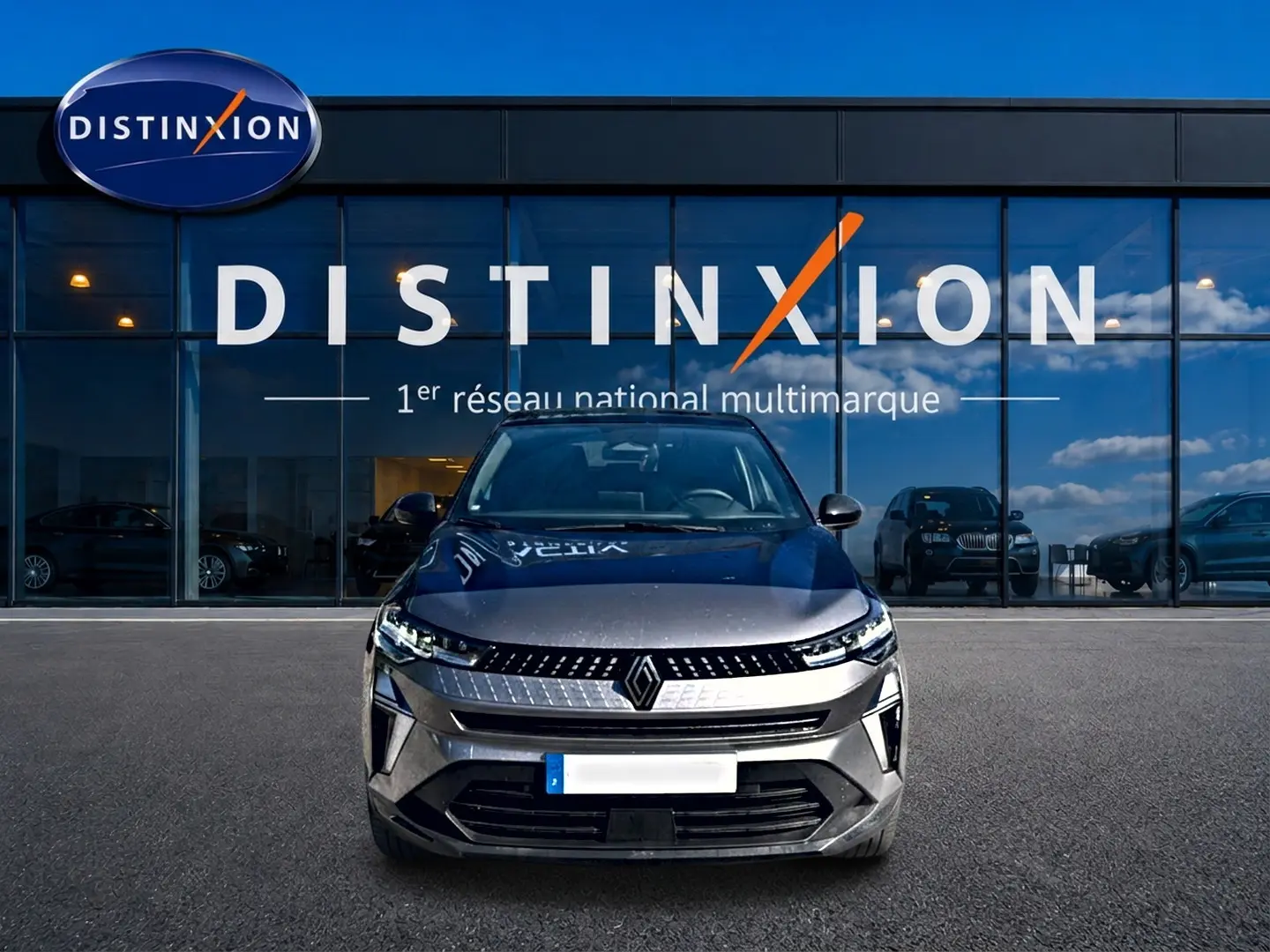 Renault Captur gris cassiopée vue de face, avec calandre moderne et phares LED allumés devant showroom Distinxion.