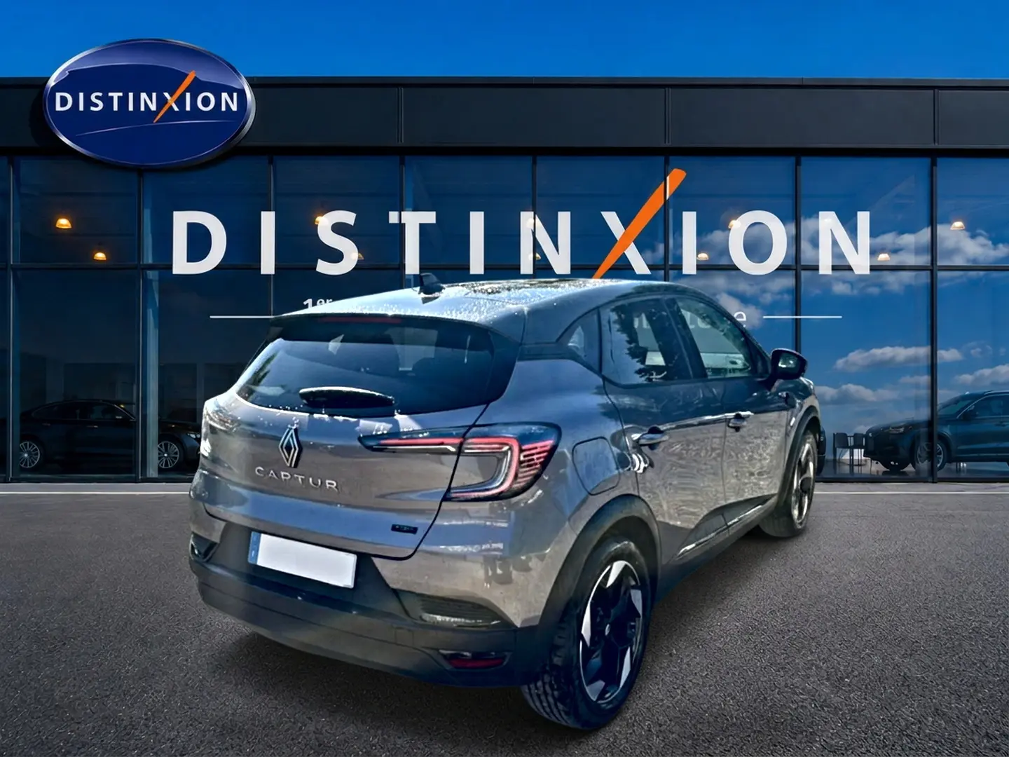Vue 3/4 arrière d'un Renault Captur gris cassiopée 2026 avec jantes alu et feux arrière LED, devant une vitrine Distinxion.