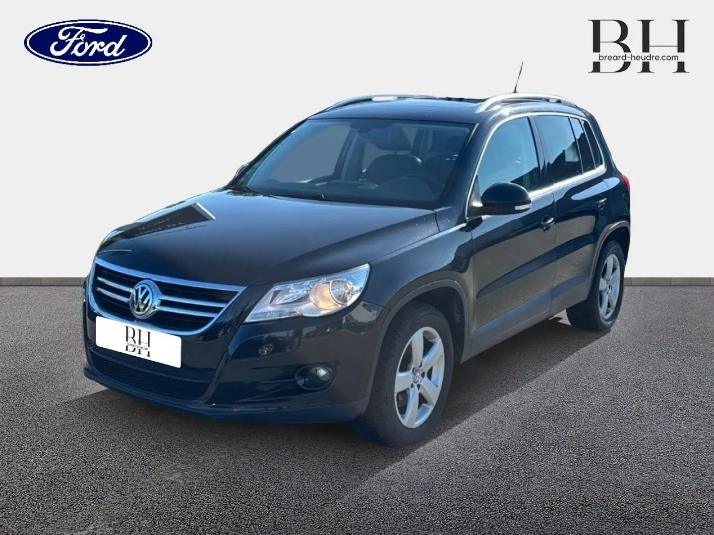 Volkswagen Tiguan noir en 3/4 avant droit, avec jantes alu et phares allumés sur fond neutre.