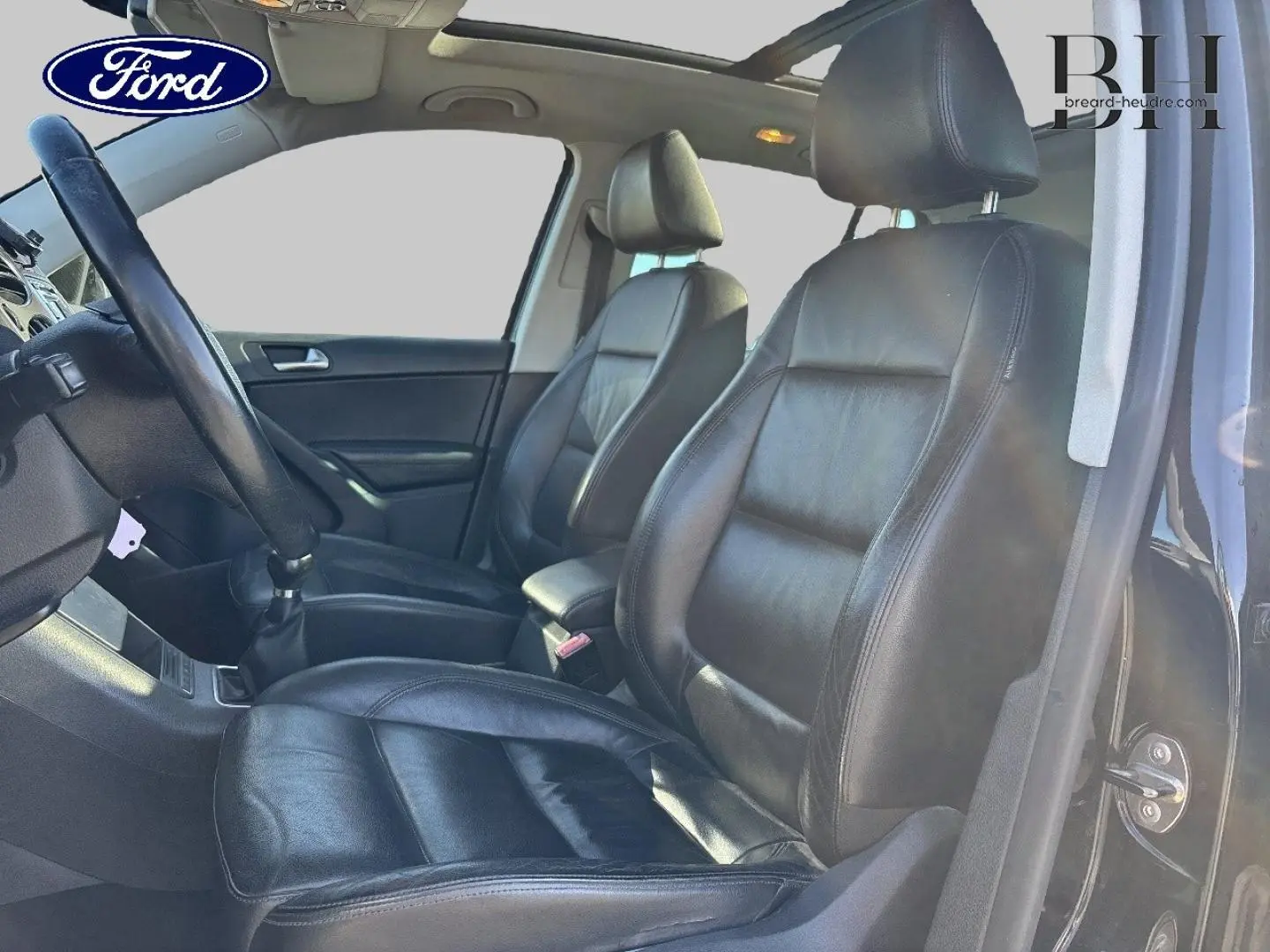 Vue intérieure côté gauche montrant les sièges avant sport en cuir noir et le volant multifonction d’un Volkswagen Tiguan beige.