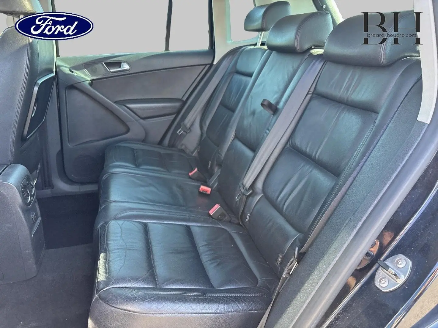 Banquette arrière en cuir noir vue côté gauche d'un Volkswagen Tiguan beige, avec ceintures de sécurité visibles.