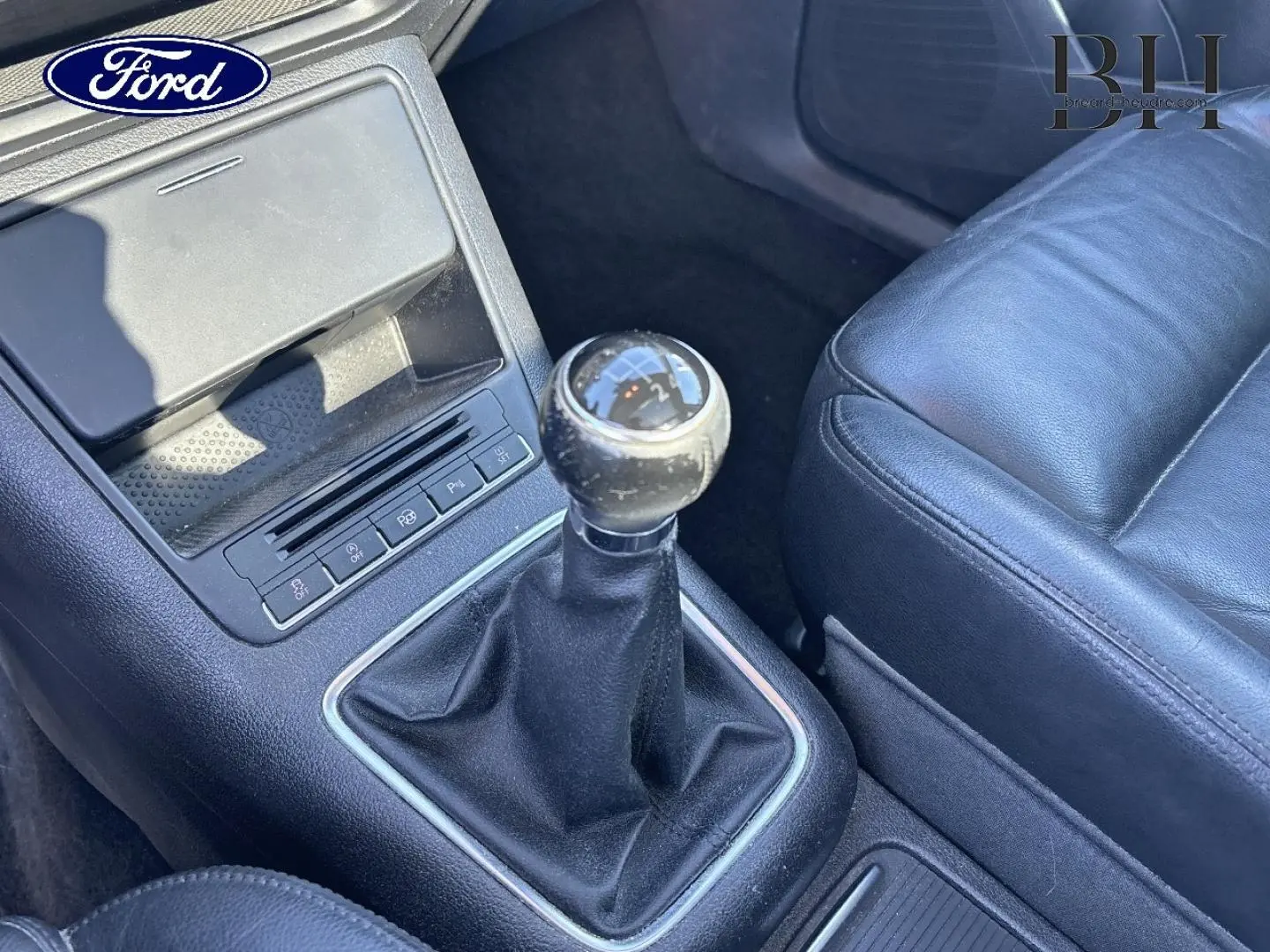 Gros plan sur la boîte manuelle et le levier de vitesse, avec siège avant en cuir noir visible à droite.