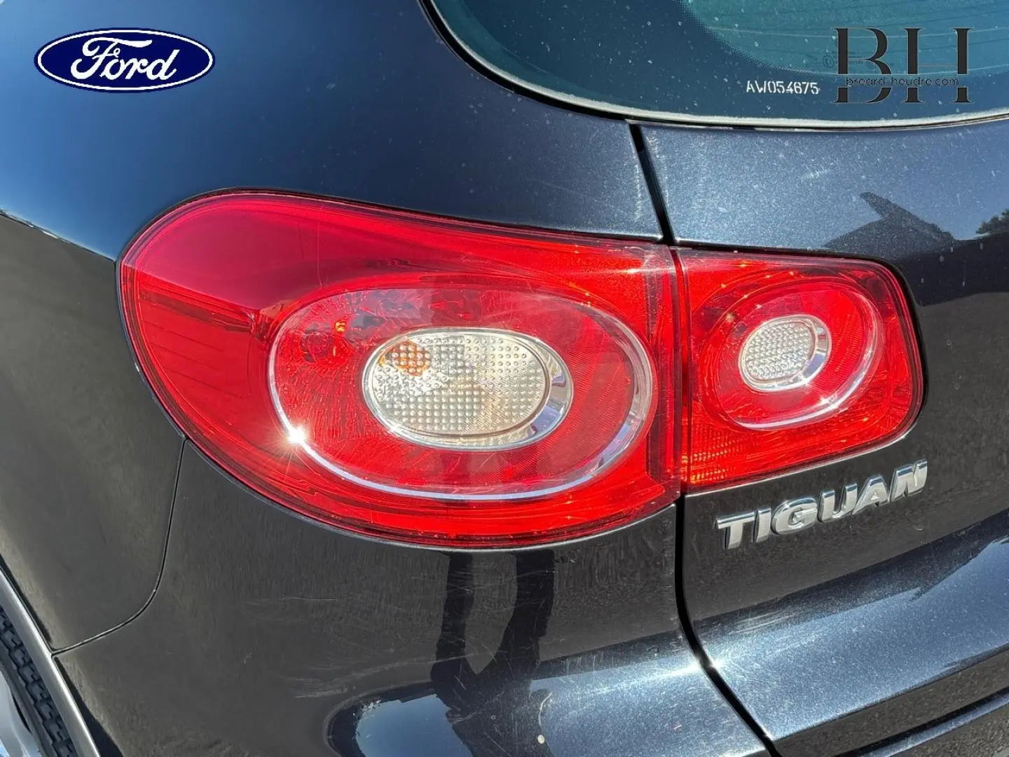 Feu arrière droit rouge sur Volkswagen Tiguan noir, gros plan sur le logo et la partie arrière du véhicule.