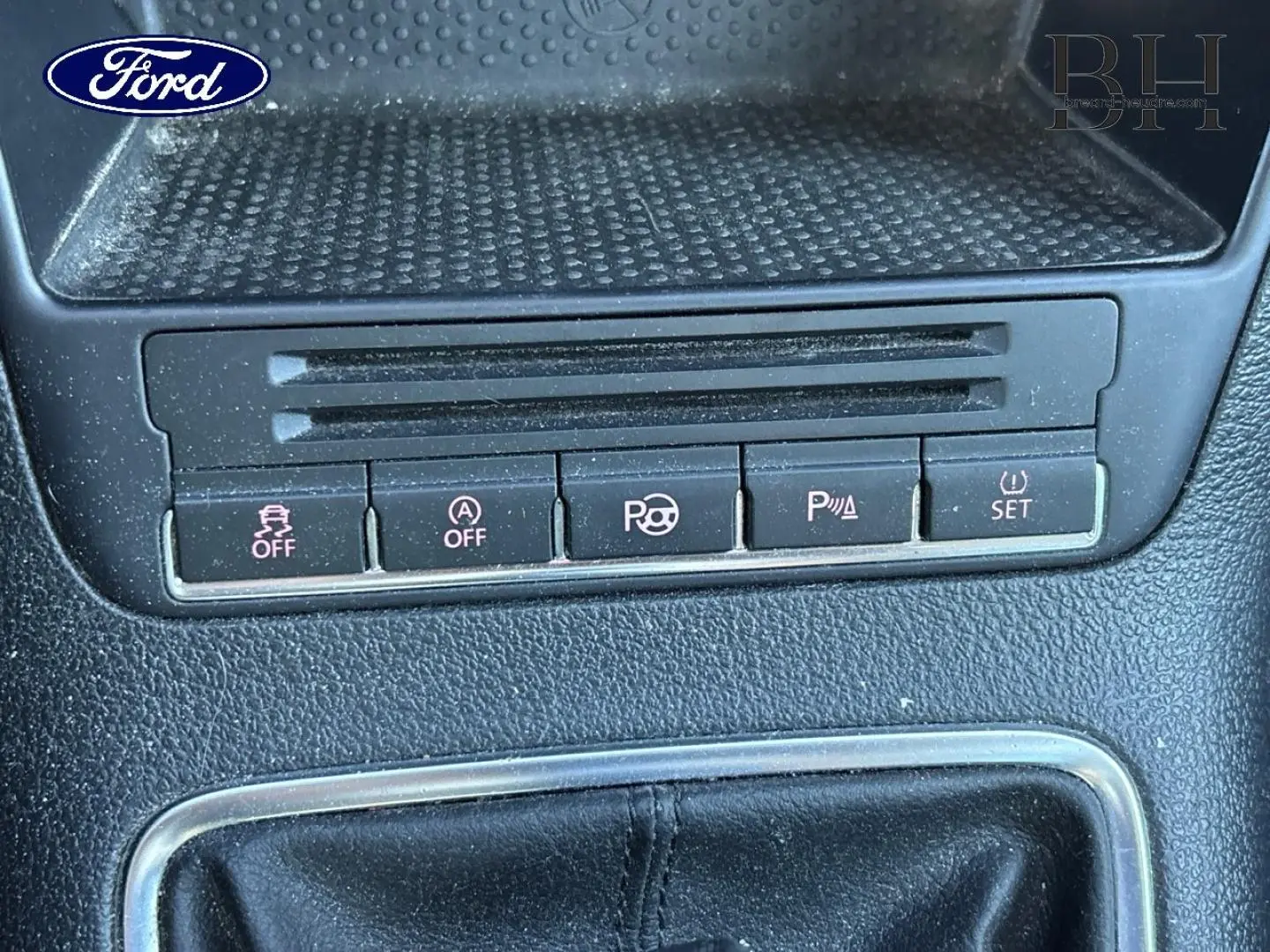 Gros plan sur la console centrale d’un Volkswagen Tiguan beige, montrant les boutons de contrôle et le soufflet de levier de vitesse en cuir noir.