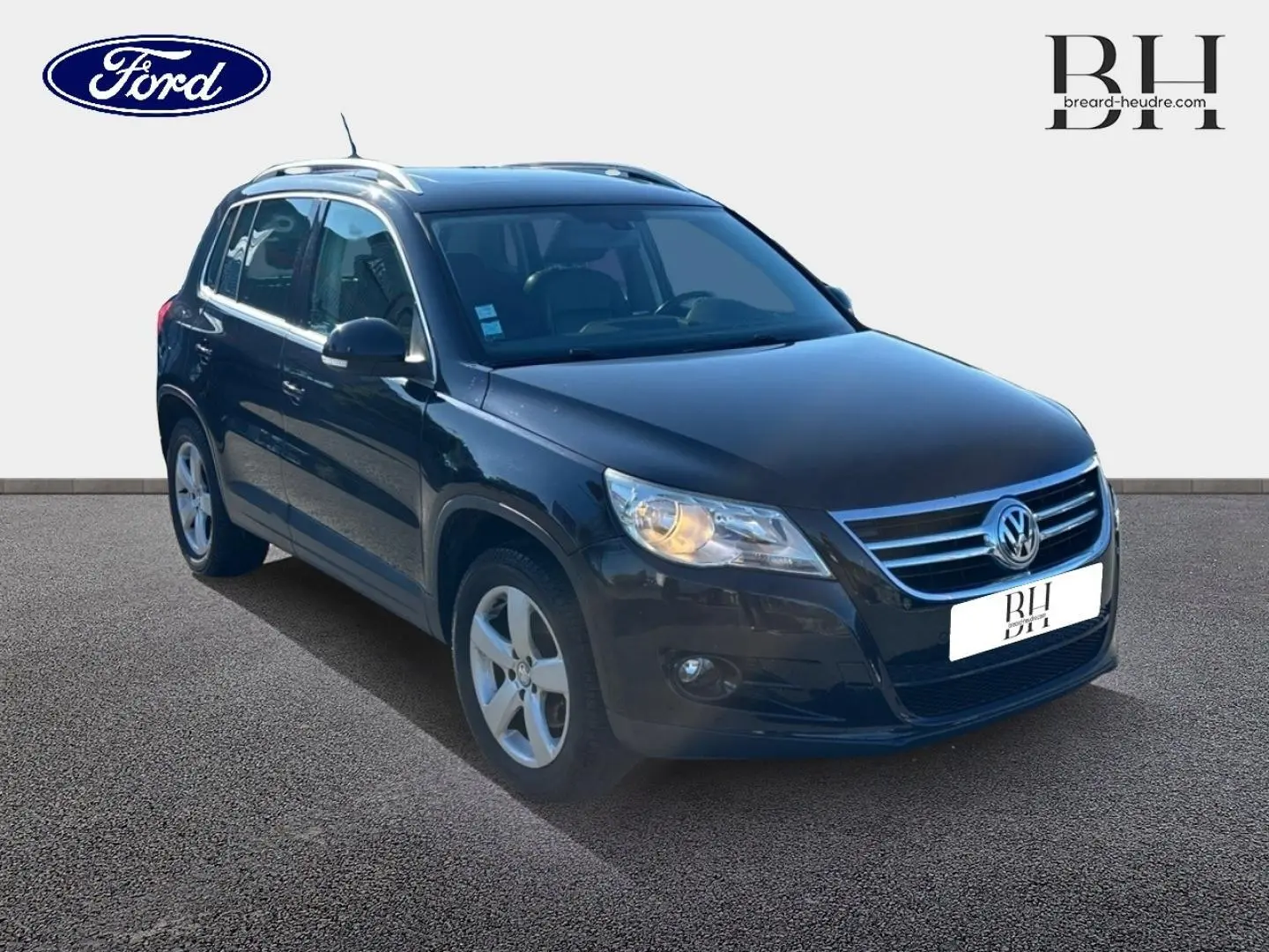 Volkswagen Tiguan noir en 3/4 avant droit, avec jantes alu et phares allumés sur fond clair.