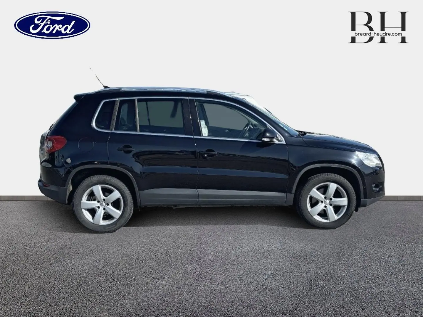 Profil côté gauche d'un Volkswagen Tiguan 2010 noir avec jantes alu et vitres teintées sur fond neutre.