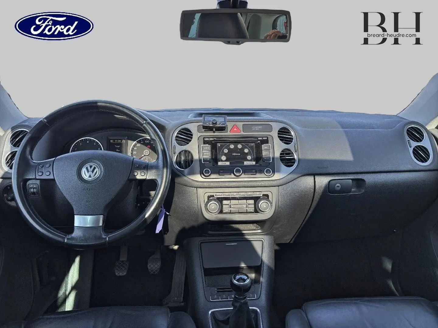 Vue intérieure avant du Volkswagen Tiguan beige 2010, volant cuir multifonction et tableau de bord avec écran central.