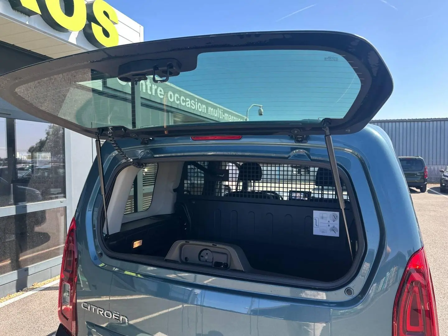 Vue arrière du Citroën Berlingo Kiama Blue avec hayon ouvert montrant l'espace de chargement et la grille de séparation.