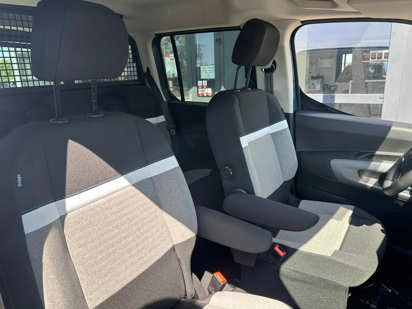 Vue intérieure avant du Citroën Berlingo 2026 avec sièges tissu bicolore gris et accoudoirs centraux.