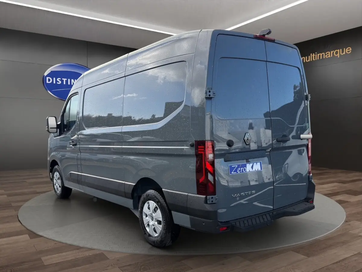 Vue 3/4 arrière droite d’un Renault Master gris foncé avec portes arrière fermées et logo visible sur fond showroom.
