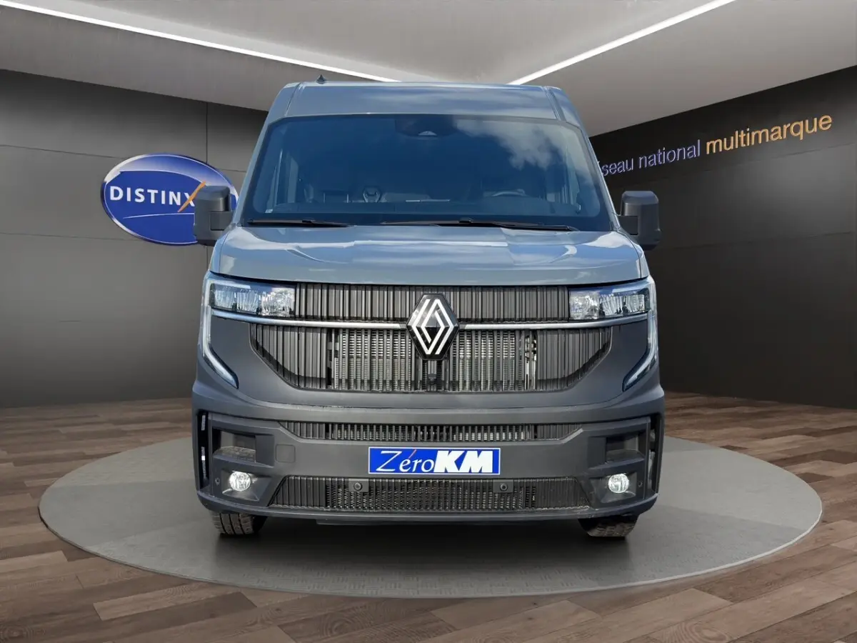 Vue avant d’un Renault Master gris avec calandre noire et feux LED, sur fond intérieur showroom multimarque.