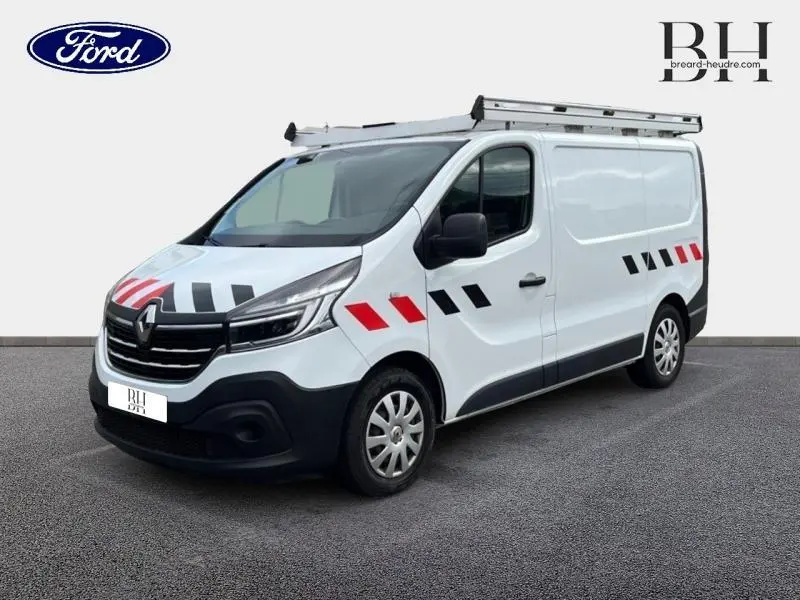 Renault Trafic Fourgon blanc glacier vu en 3/4 avant droit avec galerie de toit aluminium et marquages rouges et noirs sur la carrosserie.