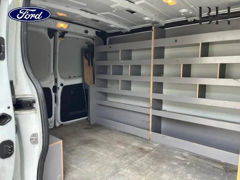 Vue intérieure arrière gauche du fourgon blanc Renault Trafic L1H1 avec étagères métalliques grises intégrées.