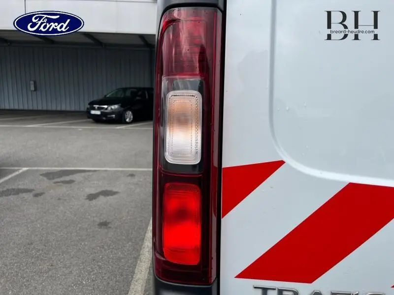 Gros plan sur le feu arrière gauche blanc et rouge du Renault Trafic Fourgon blanc Glacier avec bandes rouges réfléchissantes.