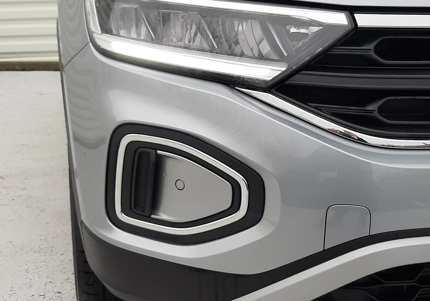 Gros plan sur l'avant gauche du Volkswagen T-Roc gris pyrite, mettant en valeur le phare et la prise d'air chromée.
