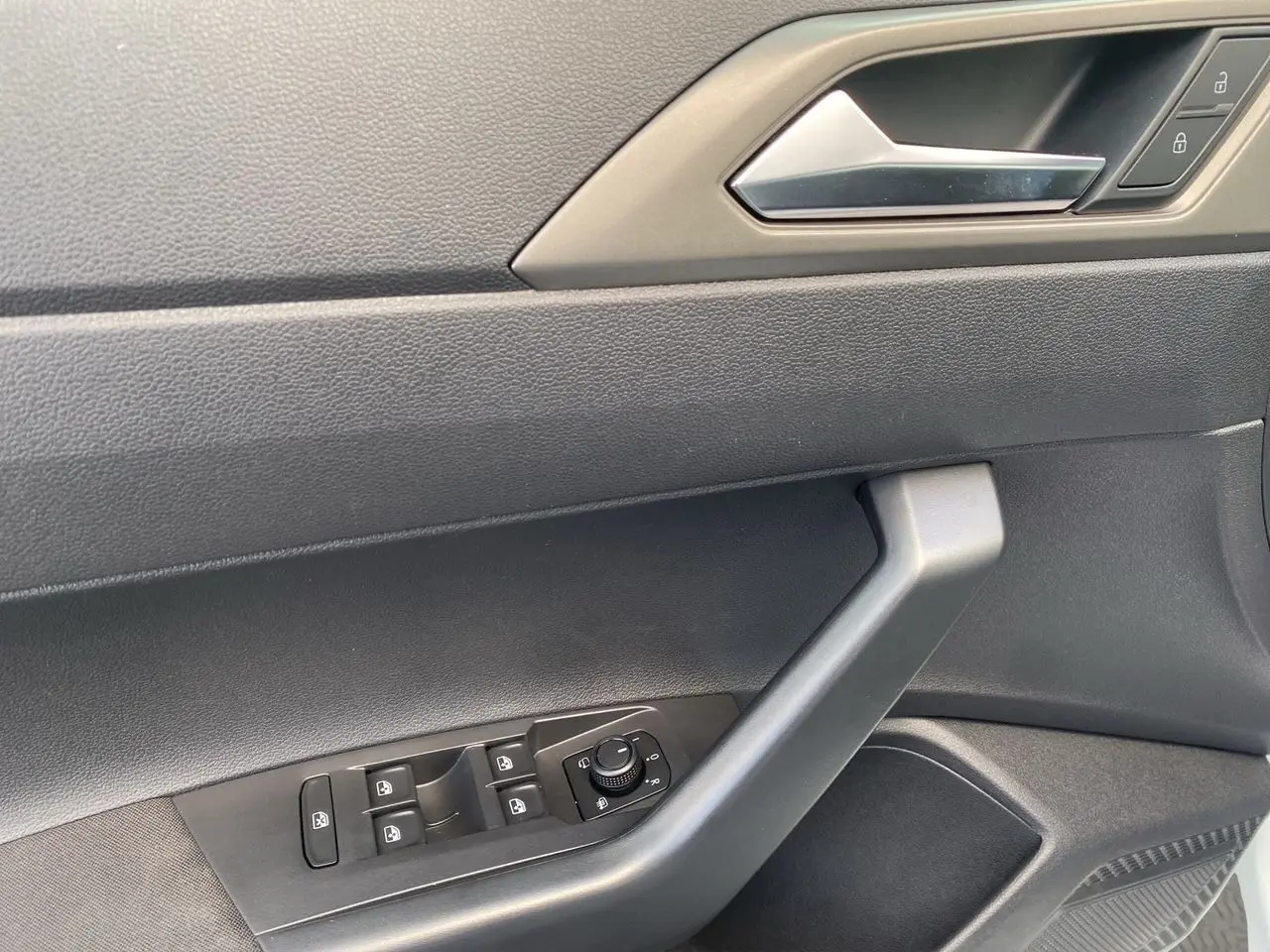Gros plan sur la porte côté conducteur de la Volkswagen Polo blanche, montrant les commandes électriques des vitres et le bouton de réglage des rétroviseurs.
