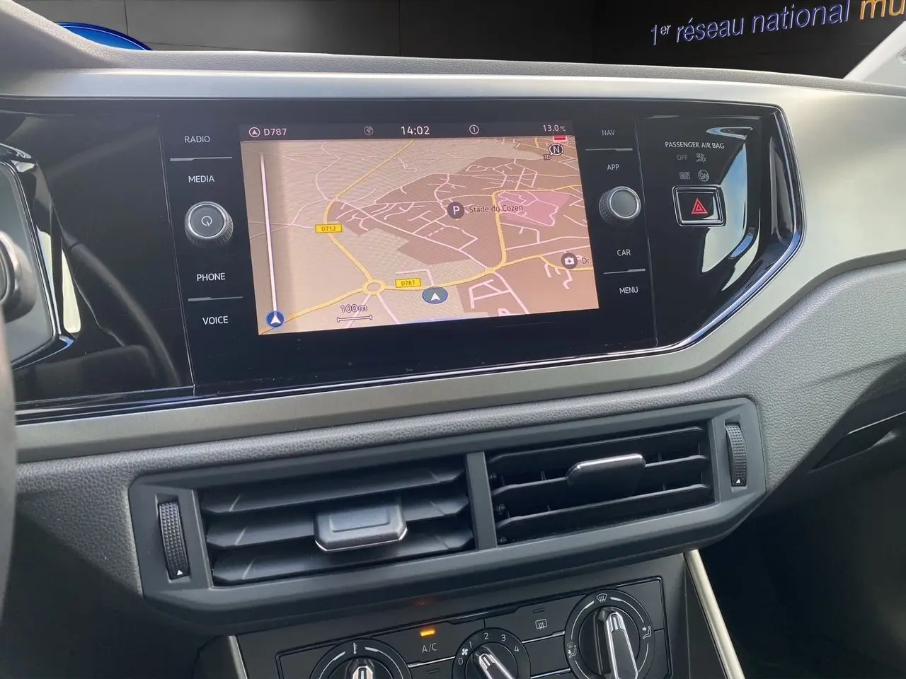 Vue rapprochée de l’écran tactile central avec navigation et commandes de climatisation d’une Volkswagen Polo blanche.