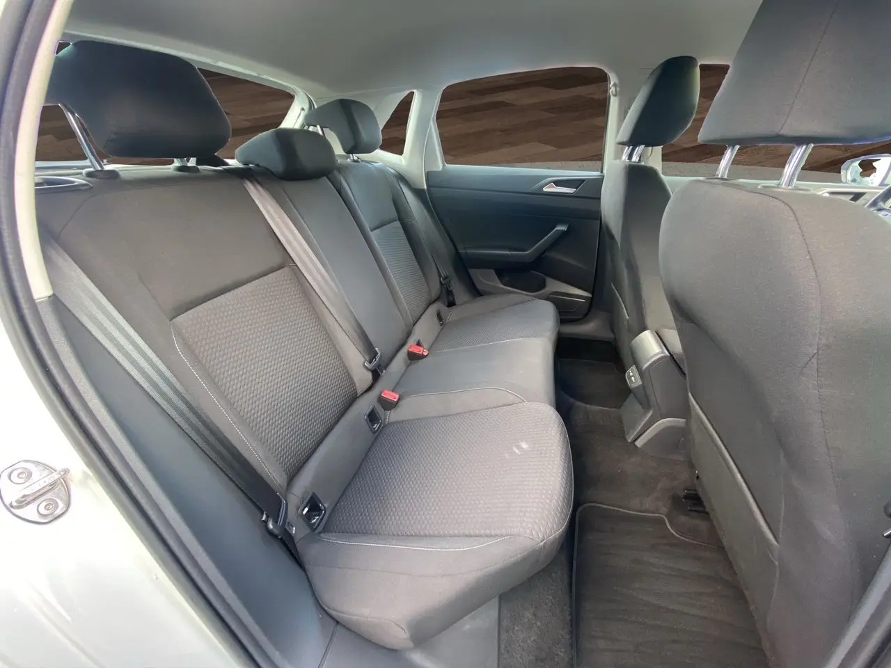 Vue intérieure arrière côté gauche de la Volkswagen Polo blanche, montrant les sièges arrière en tissu noir et les ceintures de sécurité.