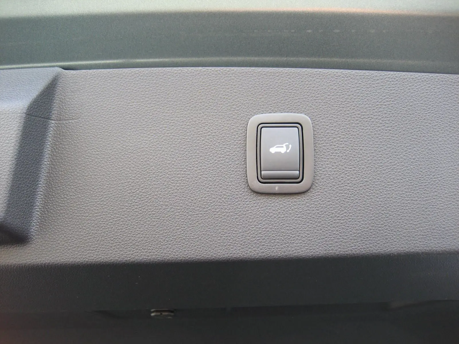 Bouton de commande d'ouverture du coffre sur le panneau intérieur d'un Dacia Bigster gris schiste.