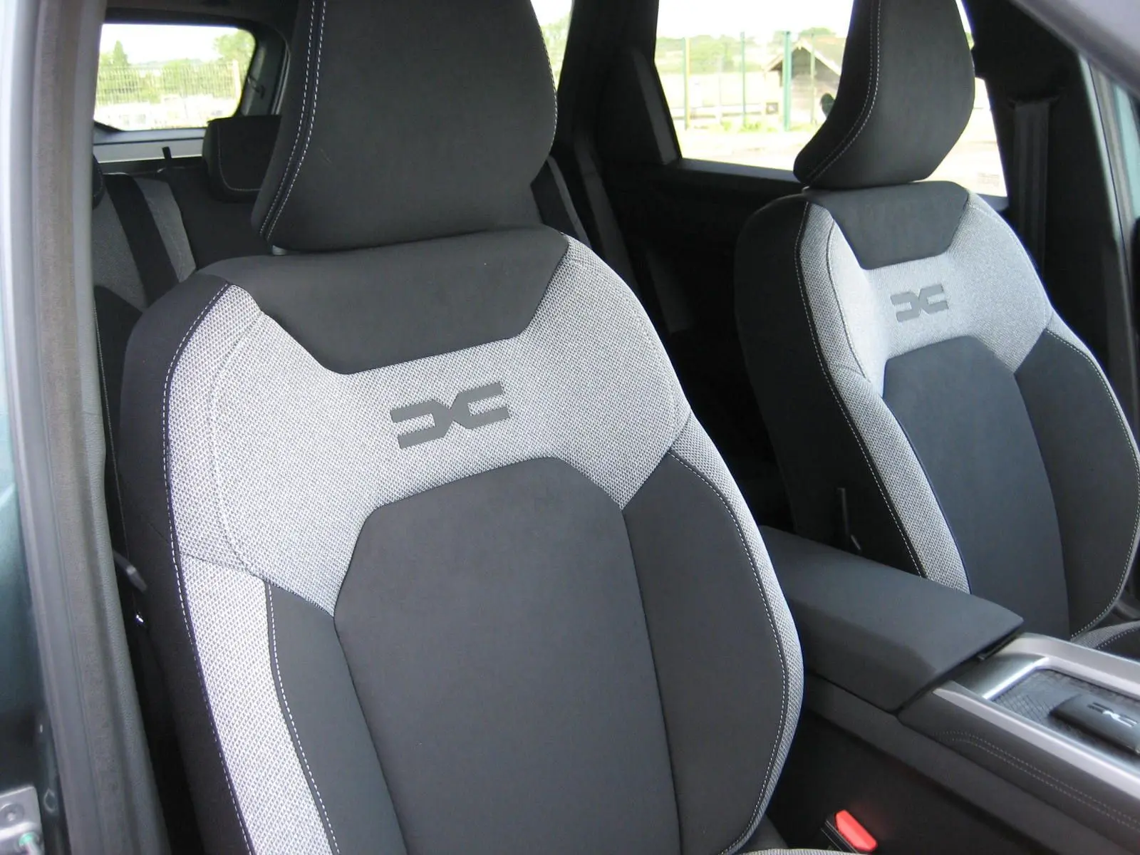 Gros plan sur les sièges avant gris clair et noir du Dacia Bigster 1.8 Hybrid 155 CH, avec logo distinctif brodé.