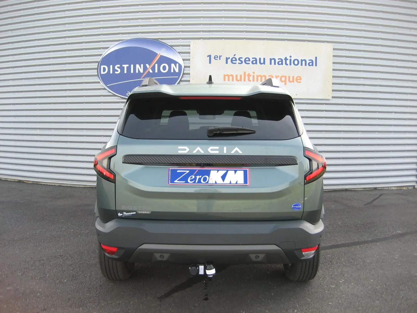 Vue arrière d'un Dacia Bigster gris schiste 2026 avec attelage et logo DACIA lumineux sur le hayon.