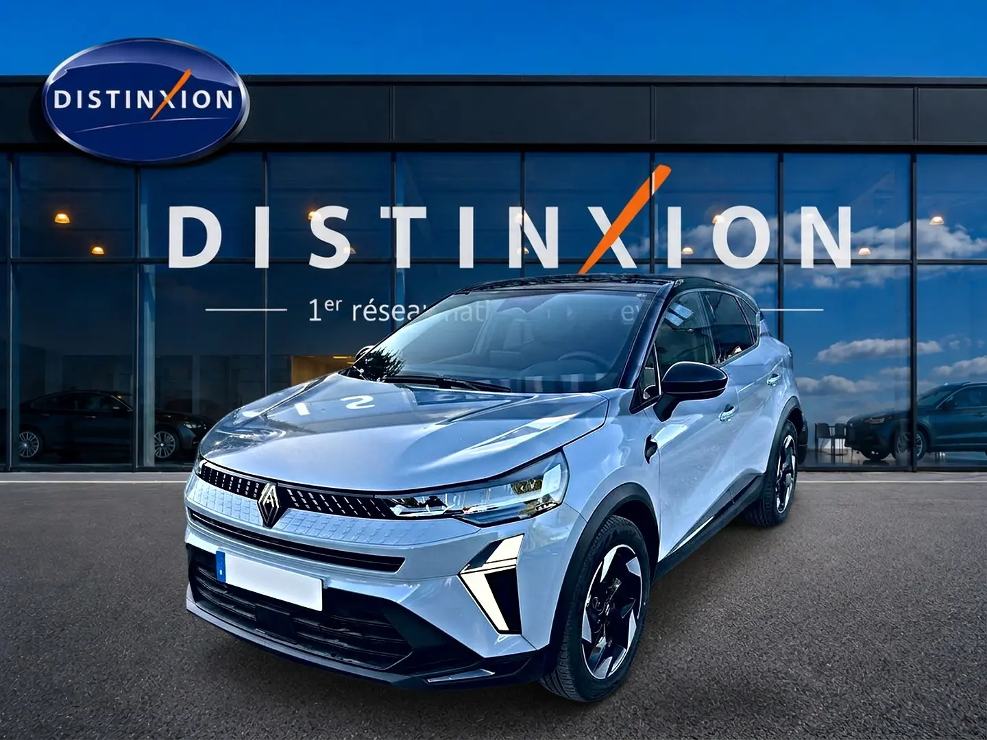 Vue 3/4 avant d'un Renault Captur gris rafale avec jantes noires et détails lumineux modernes, devant une vitrine Distinxion.