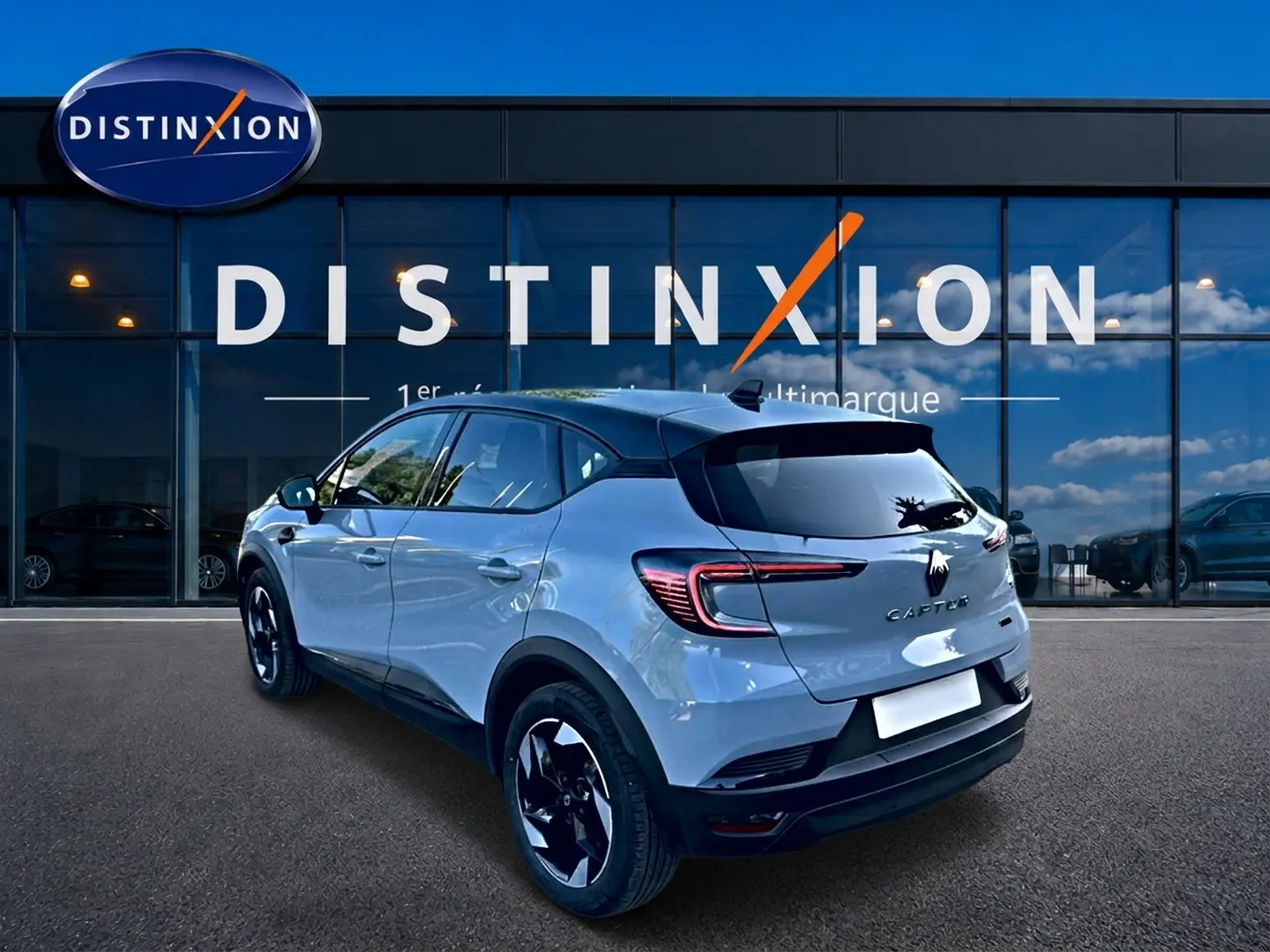 Vue 3/4 arrière droite d'un Renault Captur gris rafale avec toit noir et feux arrière LED, devant une vitrine Distinxion.