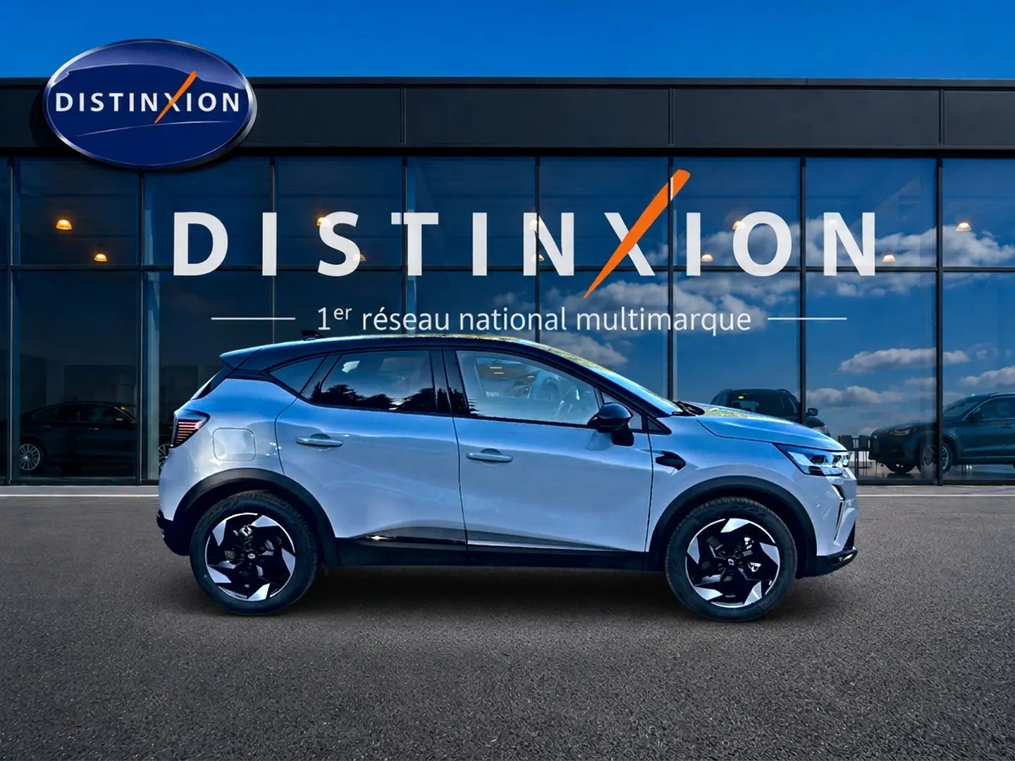 Renault Captur 1.8 e-tech hybride gris rafale en profil droit devant vitrine Distinxion, jantes noires et blanches.