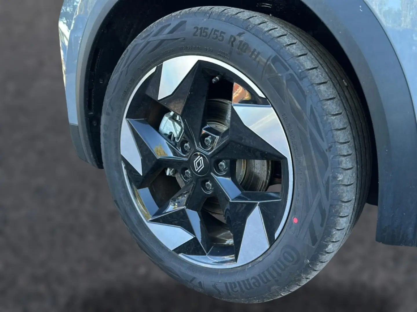 Gros plan sur la roue avant droite du Renault Captur gris rafale, mettant en valeur la jante alu noire et argentée au design géométrique.